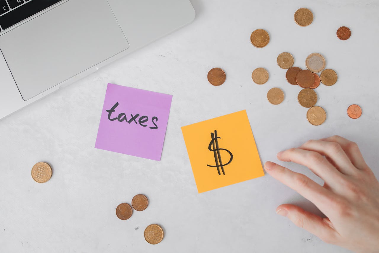 Overhead view of coins, sticky notes with tax symbols, and a hand on a desk.